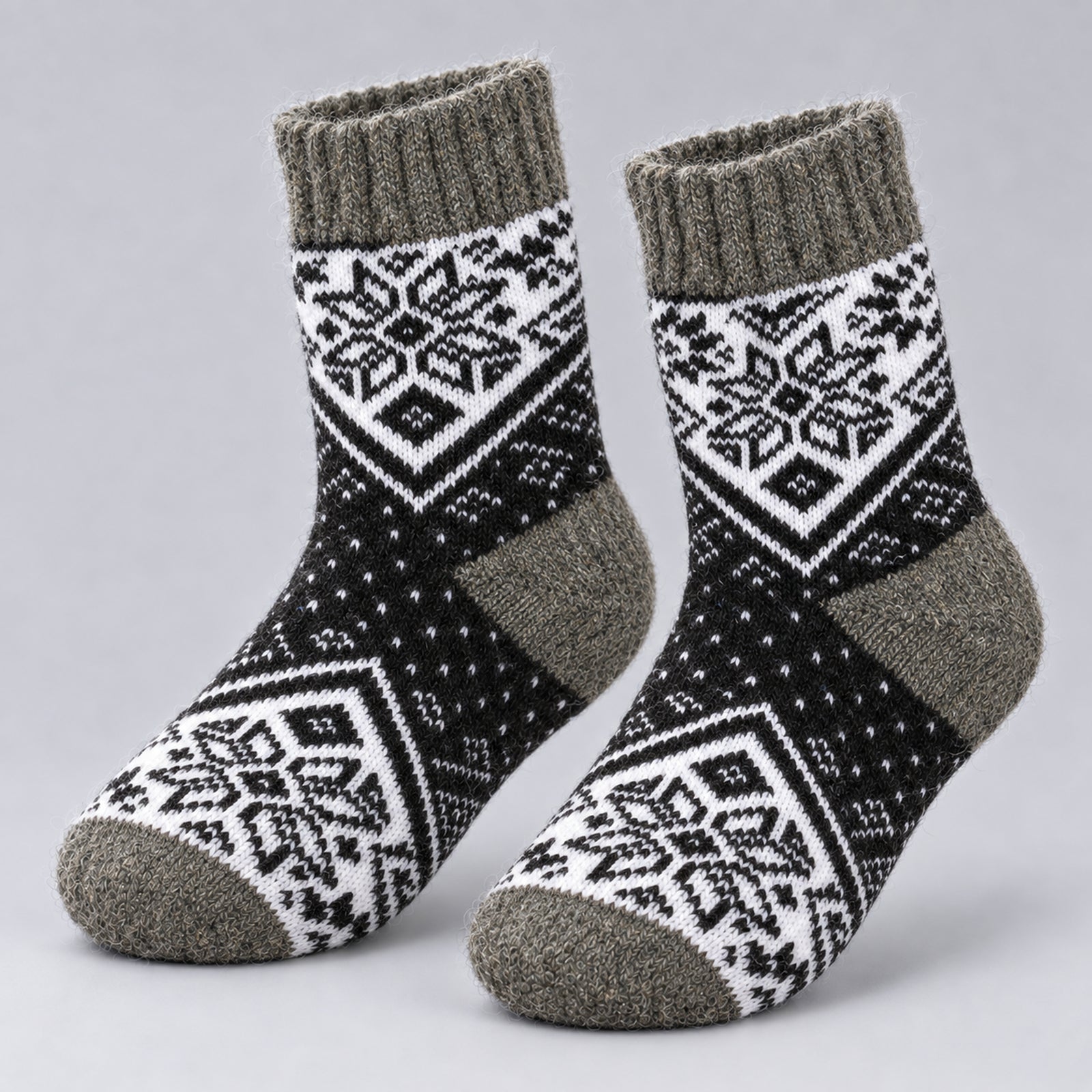 A pair of mid-calf knit socks with a black and white Nordic snowflake pattern and heather gray ribbed cuffs, heels, and toes, displayed on a light gray background.