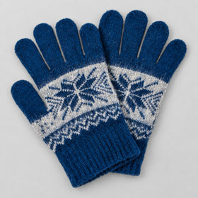 A pair of blue knit winter gloves with a white Fair Isle snowflake pattern across the back of the hands, displayed on a light gray background.