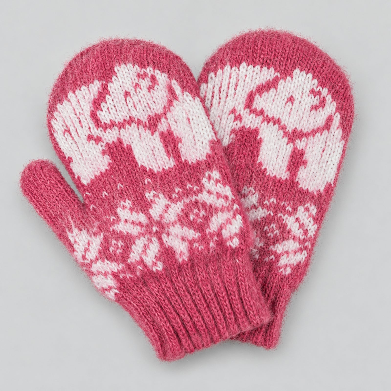 A pair of pink knit mittens with white Fair Isle patterns of polar bears and snowflakes, displayed on a neutral gray background.