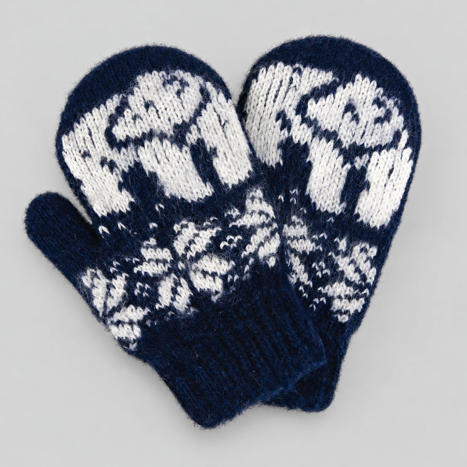 A pair of navy blue and white knit mittens with a traditional Nordic snowflake and animal pattern, displayed on a neutral gray background.