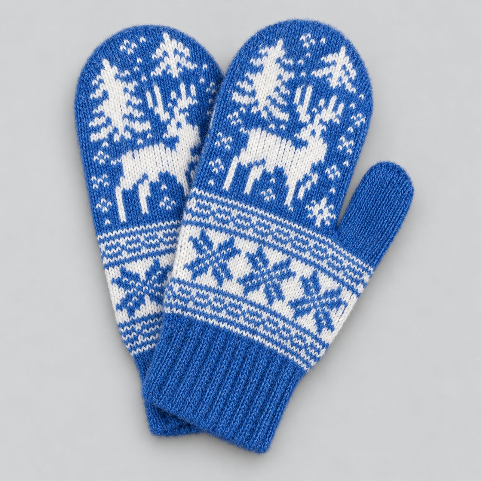 A pair of blue and white knit winter mittens with a Nordic pattern featuring reindeer, trees, and snowflakes, displayed on a neutral gray background.