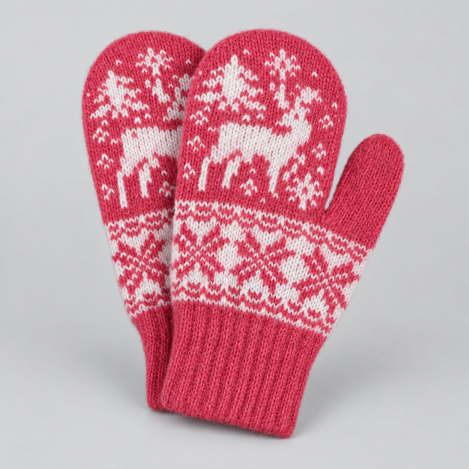 A pair of pink knit winter mittens with a white Nordic-style pattern featuring reindeer, snowflakes, and trees, displayed on a neutral light gray background.