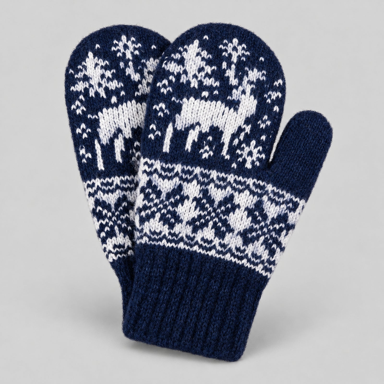 A pair of navy blue and white knit winter mittens with a fair isle pattern featuring white deer and snow trees, set against a neutral gray background.