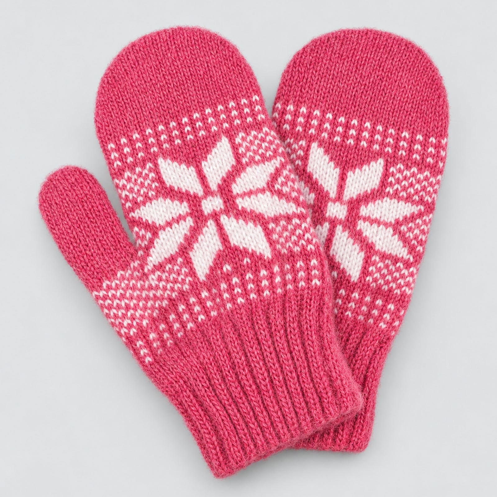 A pair of pink knit mittens with white Nordic snowflake patterns, displayed on a light gray background.