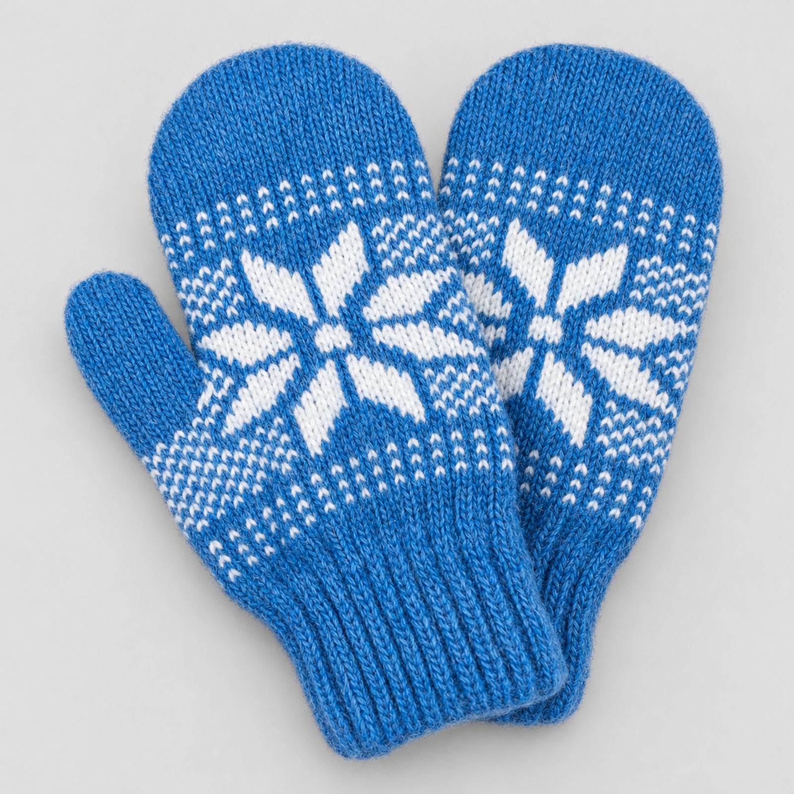 A pair of bright blue knit mittens with a white Nordic snowflake pattern, displayed on a light gray background.
