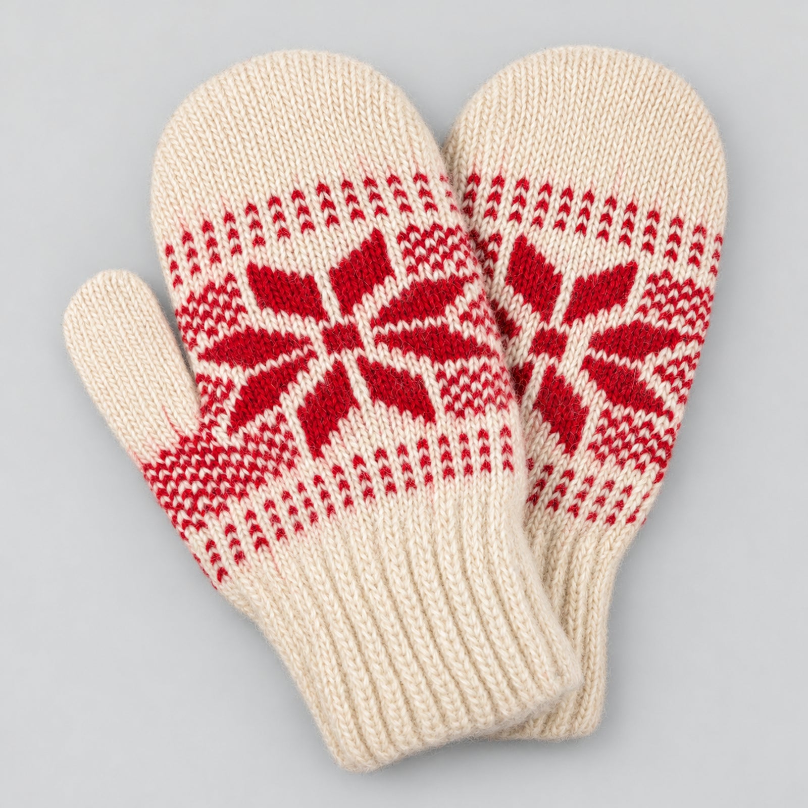A pair of cream-colored knit mittens with a red Nordic snowflake pattern, displayed on a neutral gray background.