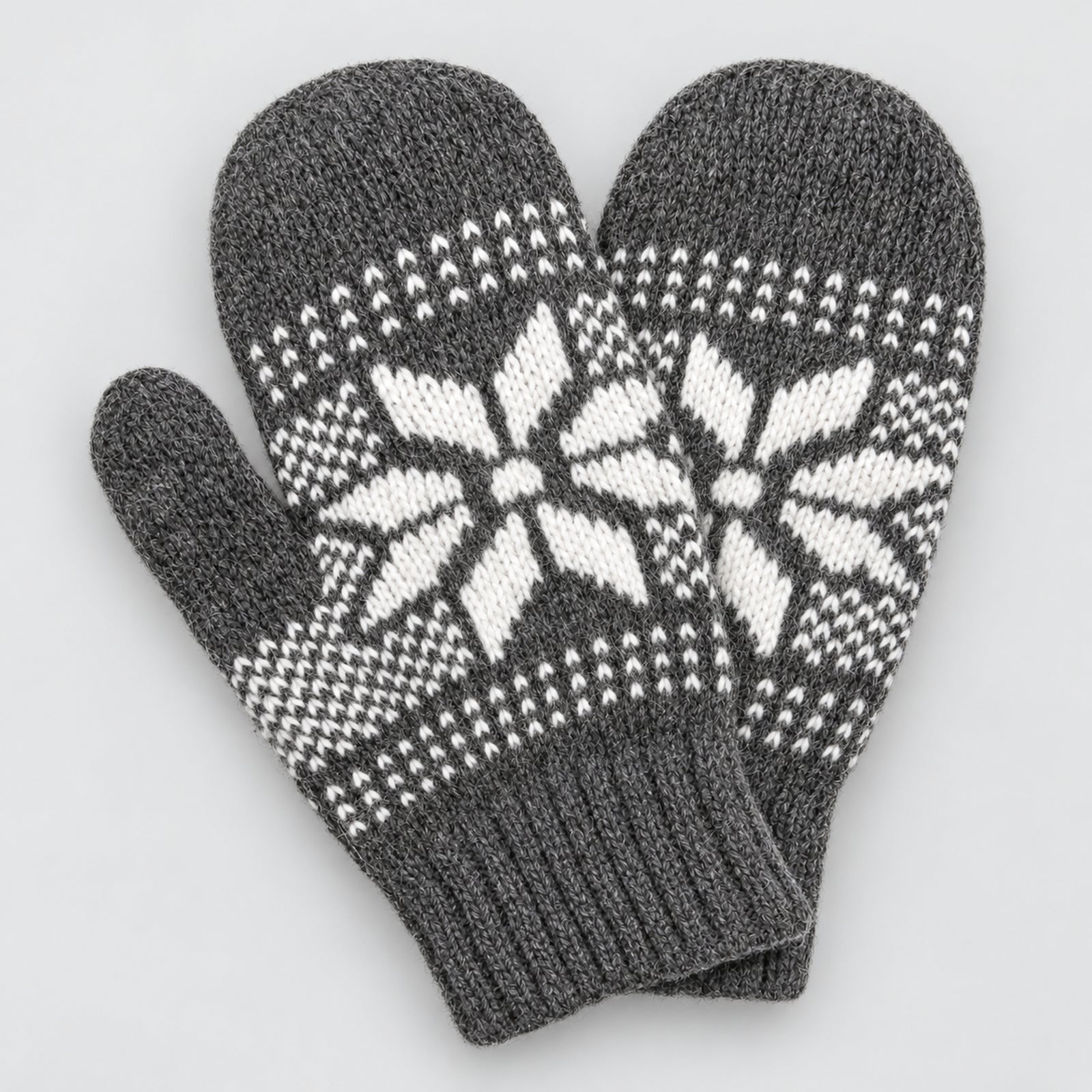 A pair of dark gray knit winter mittens with a white Nordic snowflake pattern on the back of the hands and ribbed cuffs, shown on a light gray background.