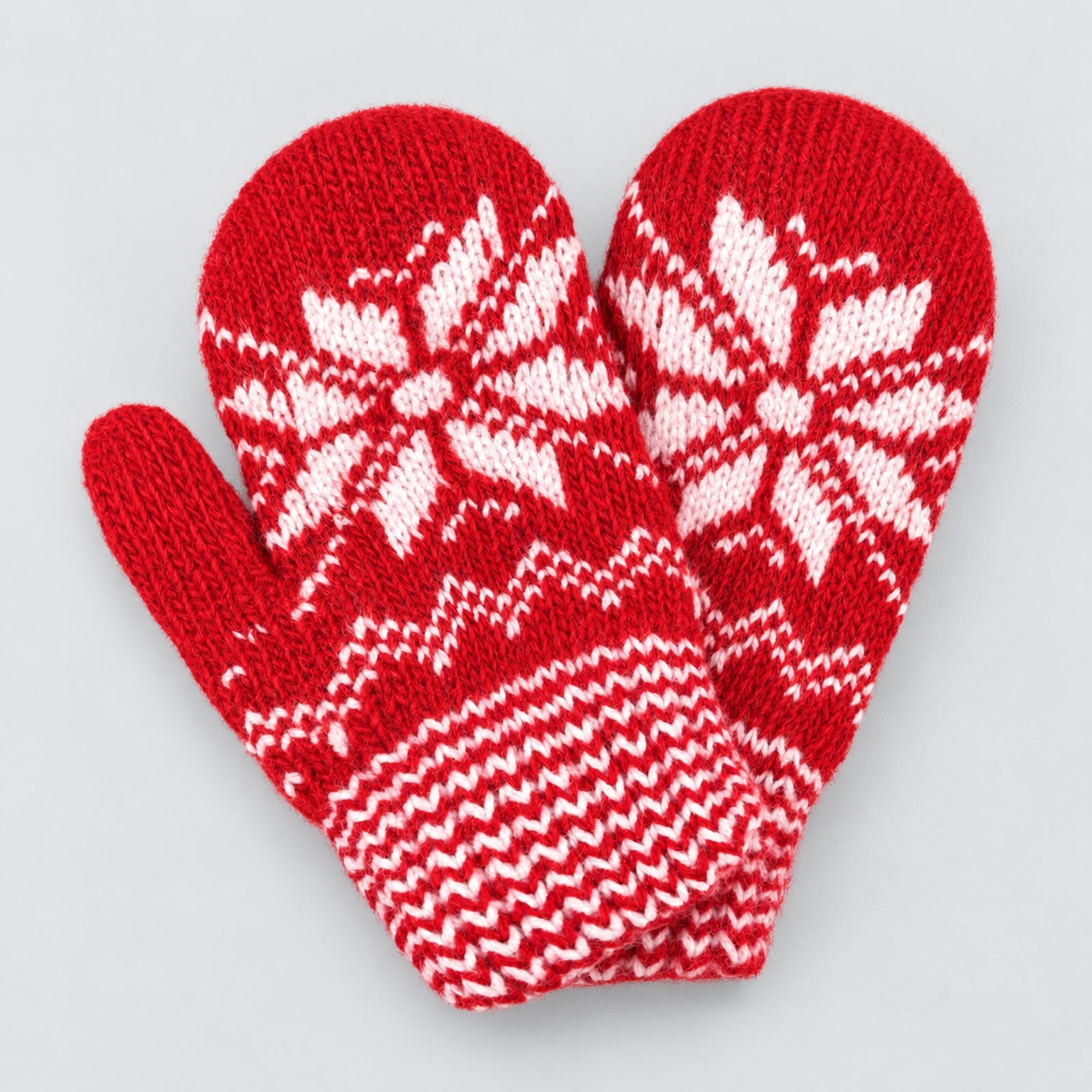 A pair of red knit mittens with white Nordic snowflake and geometric patterns, displayed against a light gray background.
