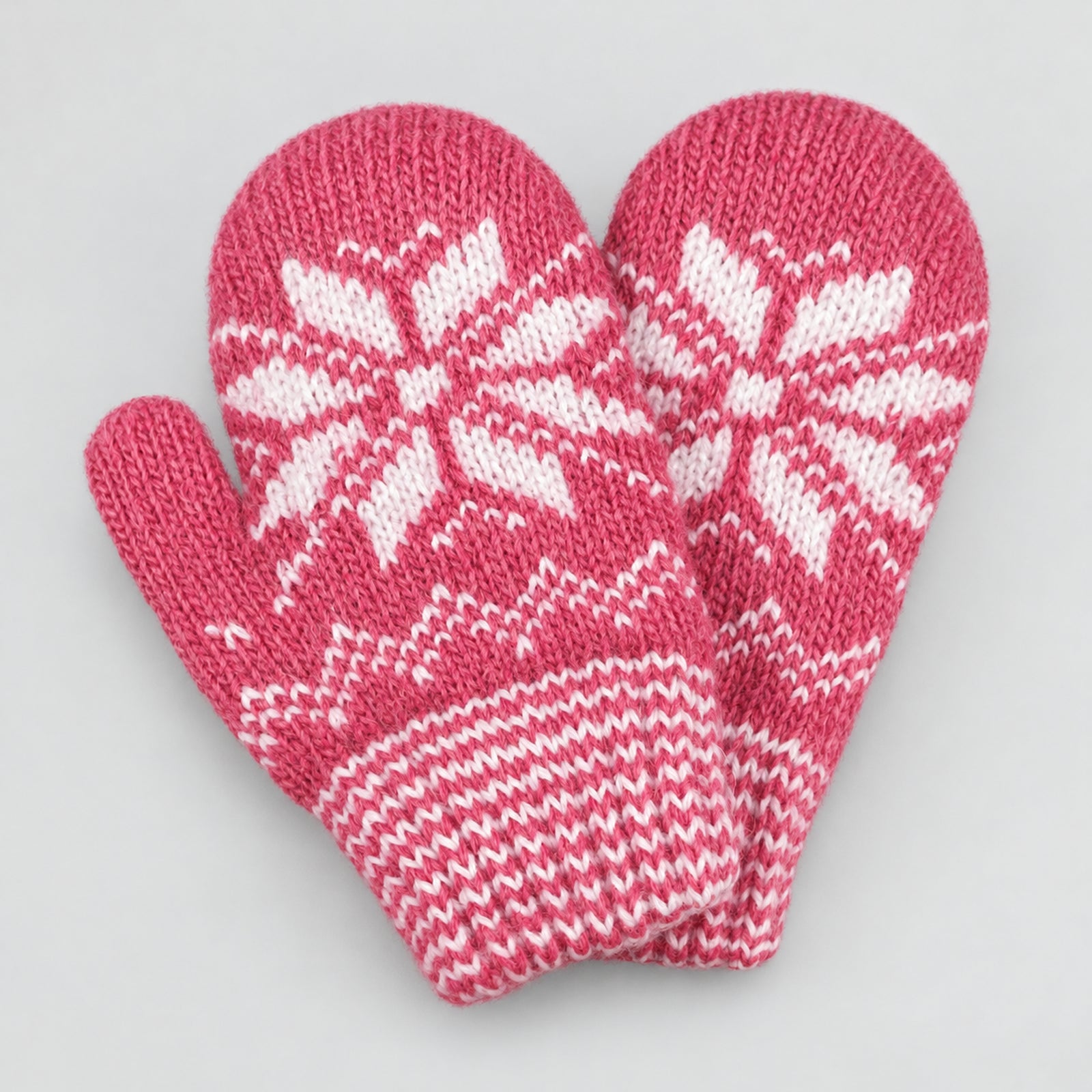 A pair of pink knit mittens with white snowflake and geometric patterns, displayed on a light gray background.