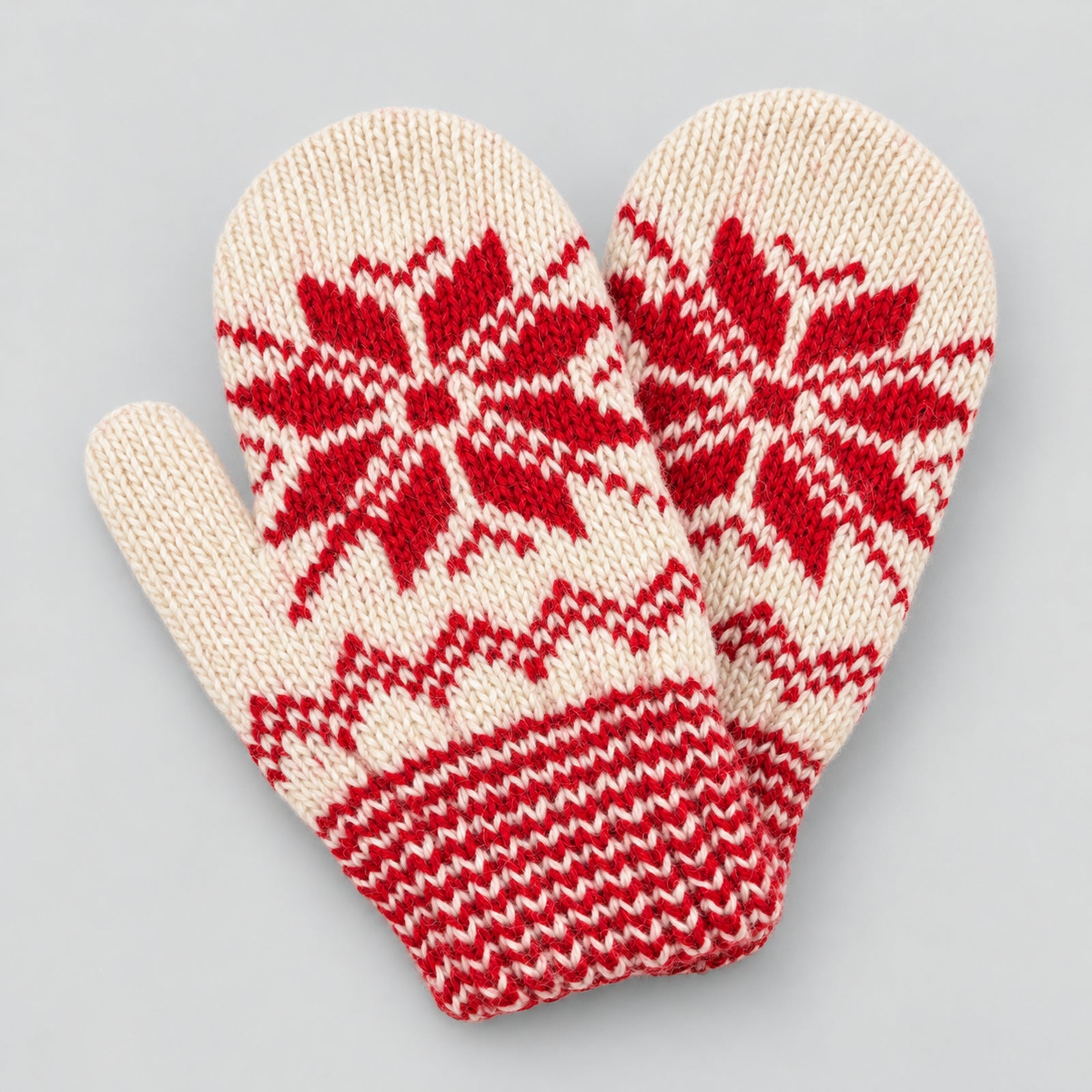 A pair of cream-colored knit mittens with a red Nordic snowflake and chevron pattern, displayed on a neutral light gray background.
