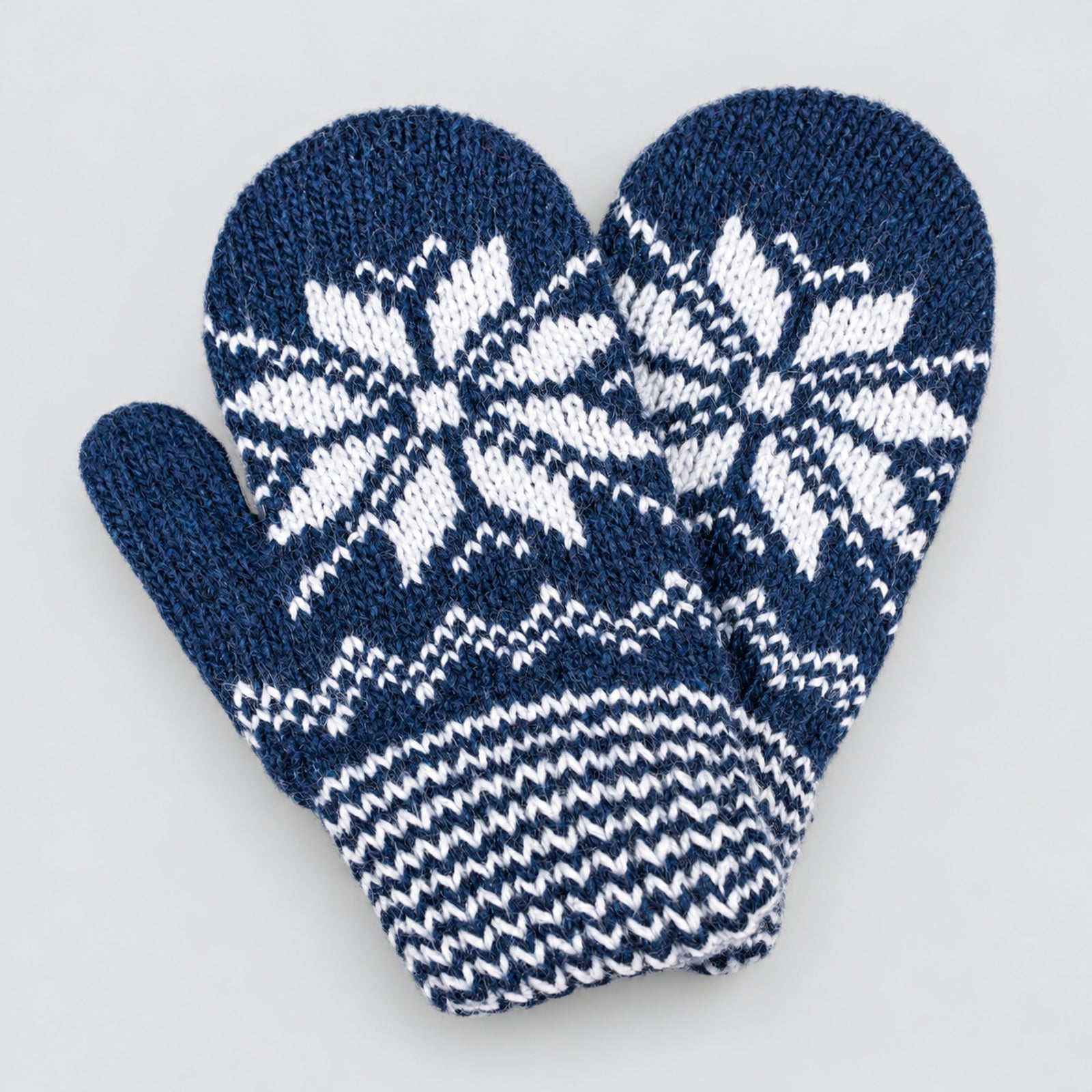 A pair of navy blue and white knit mittens with a snowflake pattern and chevron cuff, shown on a light gray background.