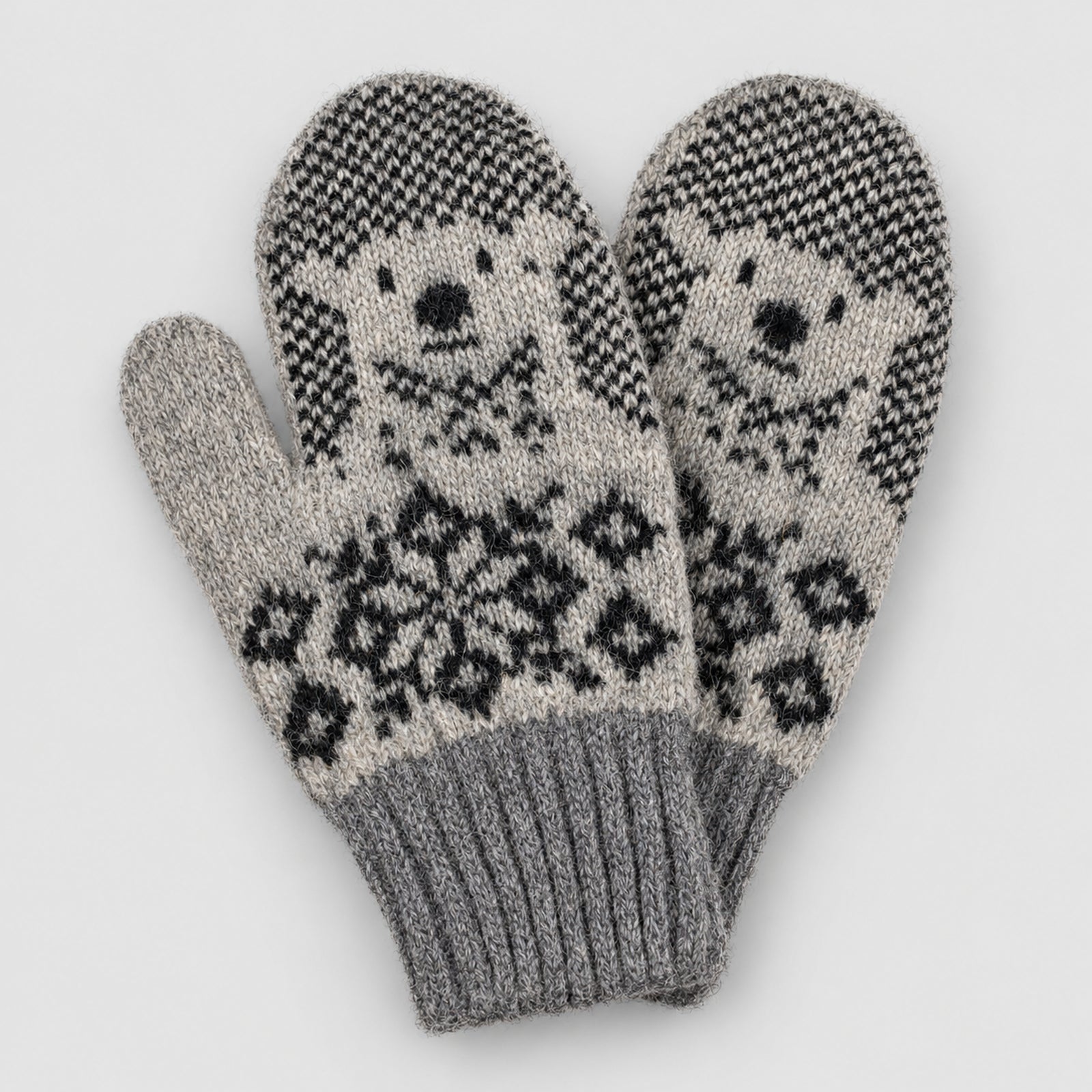 A pair of knit winter mittens in gray and black, featuring a polar bear face pattern on the back of the hands and a snowflake motif on the palms, set against a light gray background.