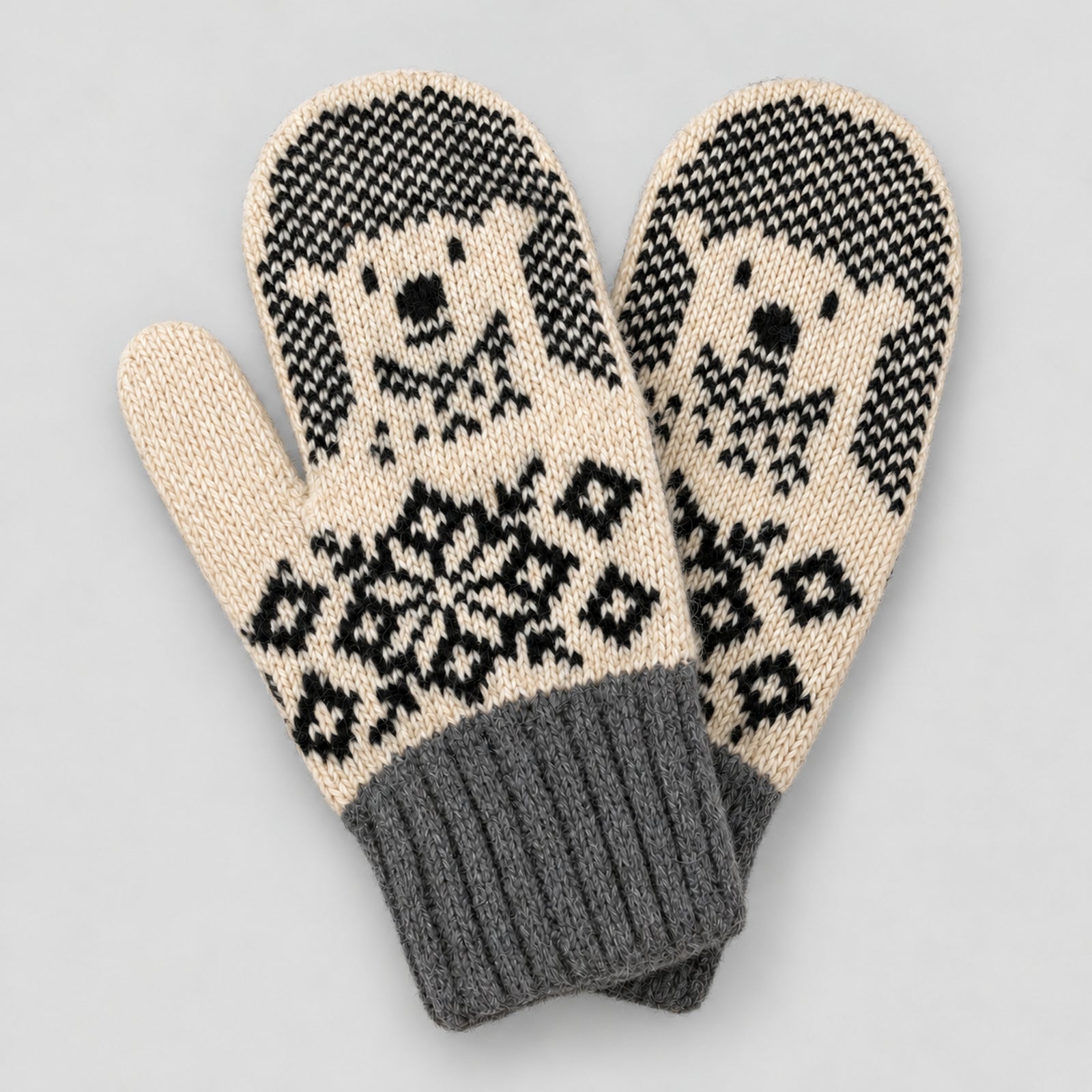 A pair of knit winter mittens with a black and cream dog face pattern and a gray ribbed cuff, shown on a light gray background.