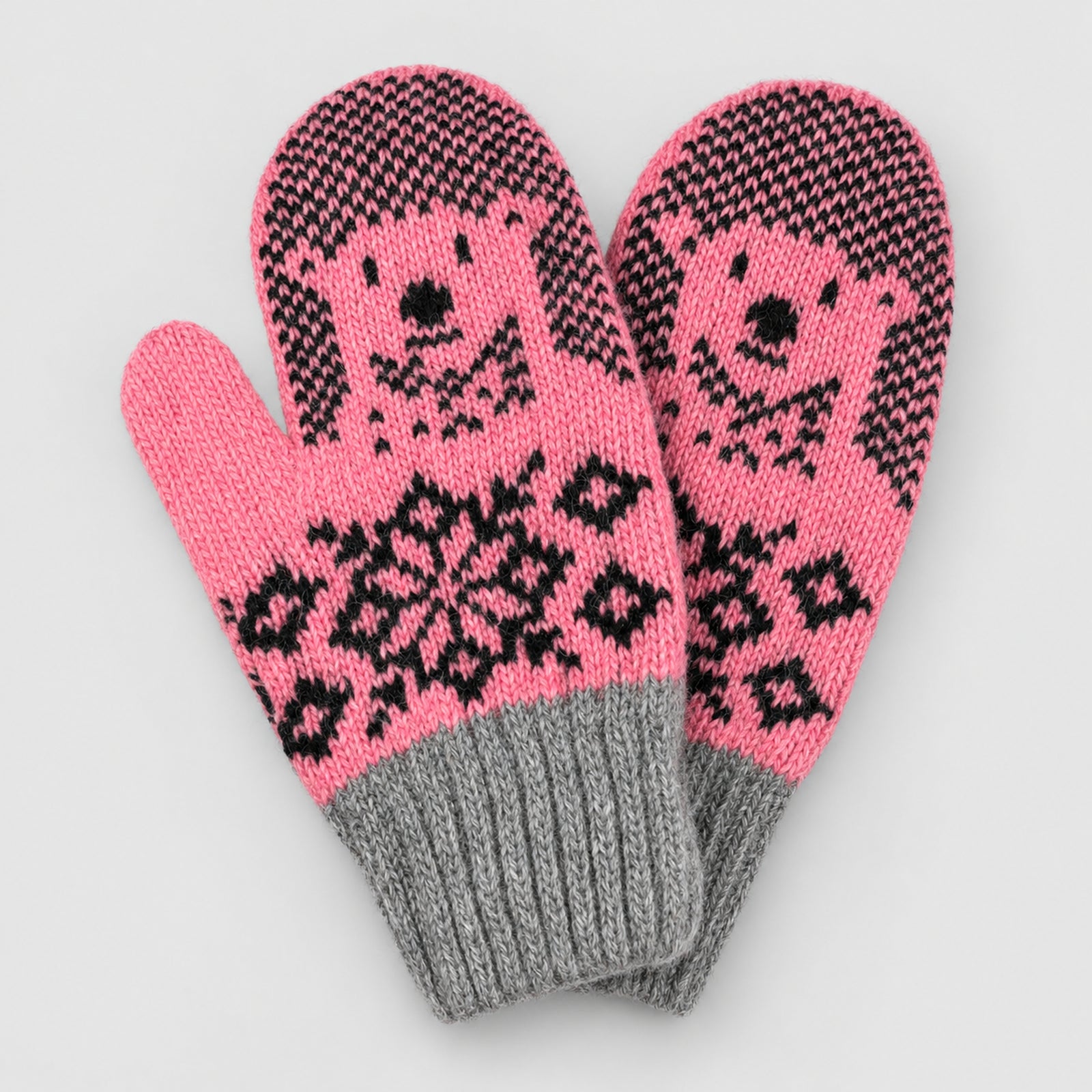 A pair of pink knit winter mittens with black Nordic-style patterns and a gray ribbed cuff, shown on a light gray background.