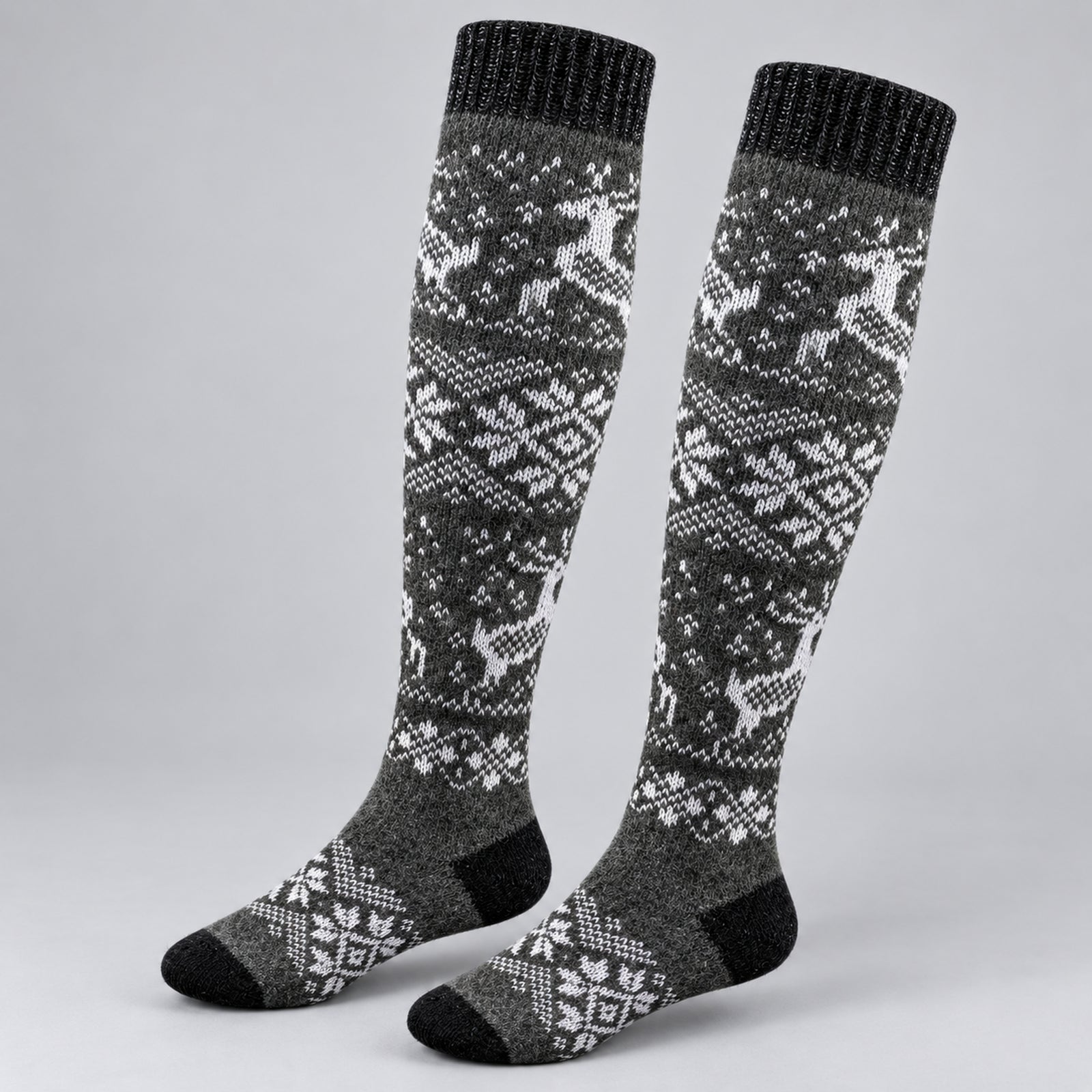 A pair of knee-high knit socks with a gray and white Nordic/Fair Isle pattern featuring reindeer and snowflakes, shown on a light gray background.