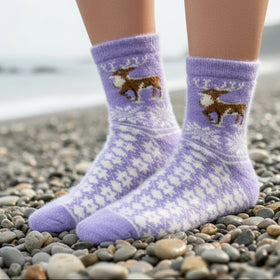 Purple knitted sock with a deer design on a pebbly beach.