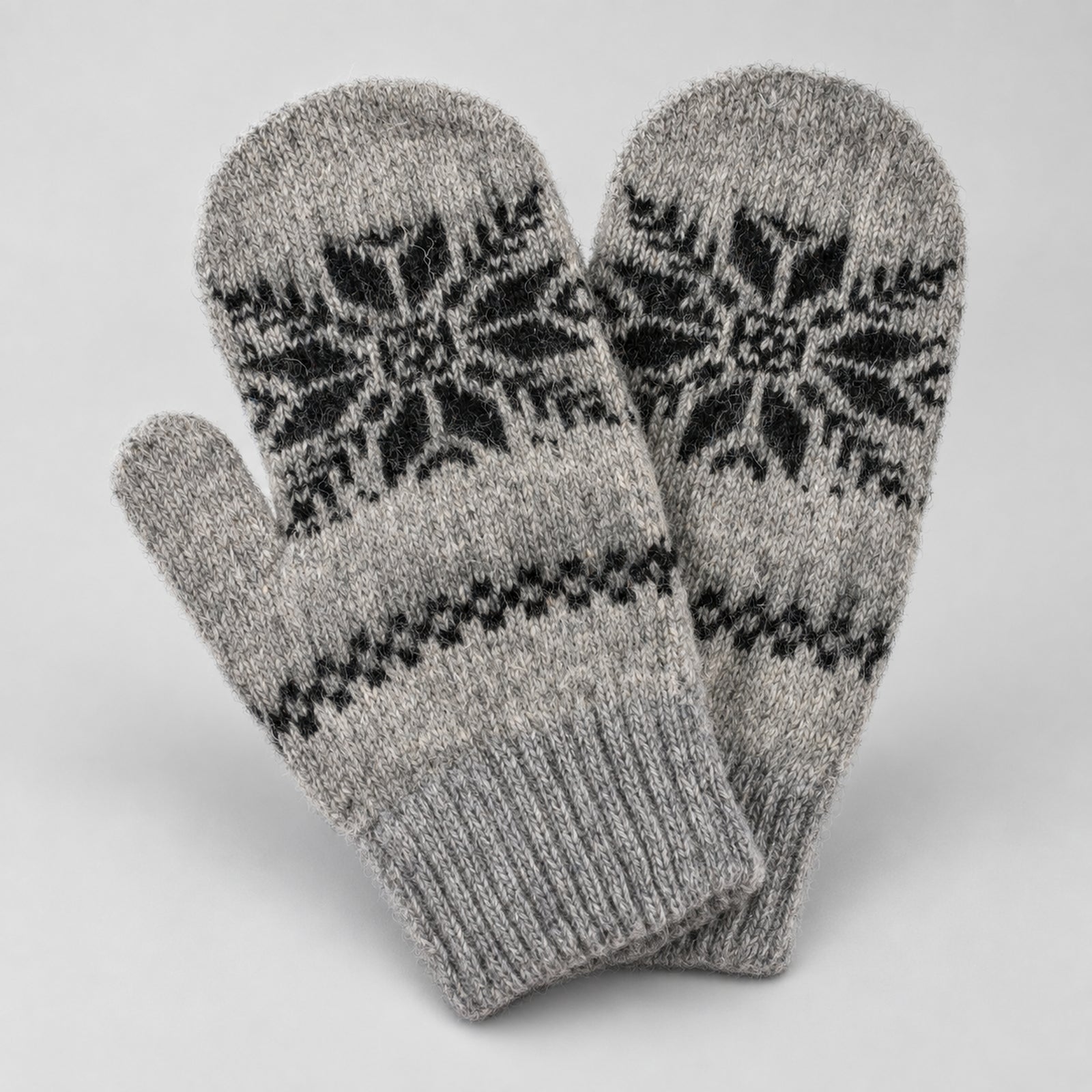 A pair of gray knit mittens with black Fair Isle snowflake and geometric patterns, displayed against a light gray background.