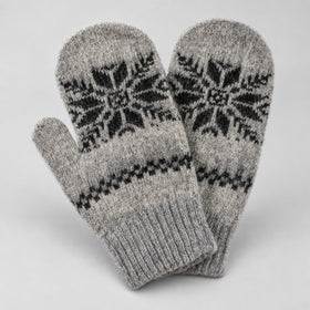 A pair of gray knit mittens with black Fair Isle snowflake and geometric patterns, displayed against a light gray background.