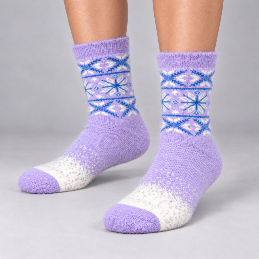 A pair of purple knit crew socks with blue and white Fair Isle snowflake patterns and a white toe, shown on a model's feet against a gray studio background.