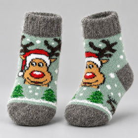 A pair of gray knit socks with a festive Christmas design featuring a reindeer wearing a Santa hat, green Christmas trees, and white snowflakes on a light sage green background.