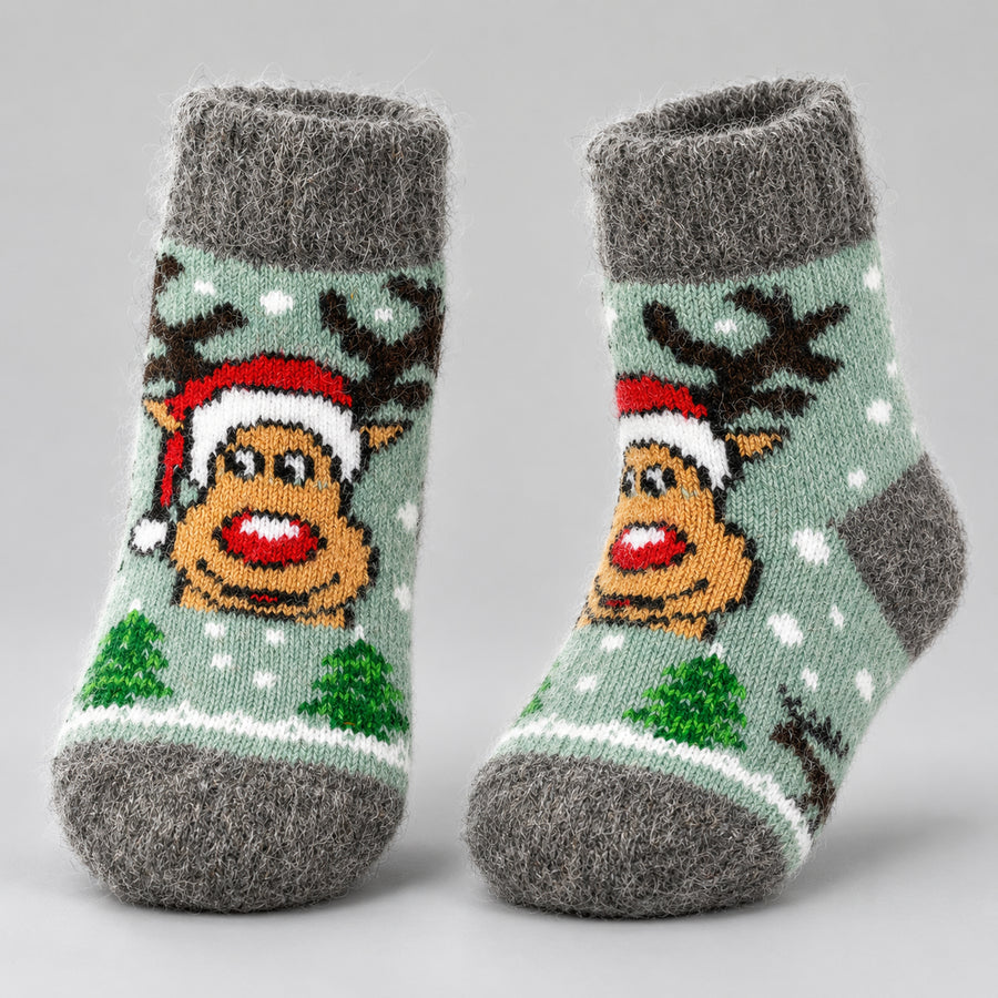 A pair of gray knit socks with a festive Christmas design featuring a reindeer wearing a Santa hat, green Christmas trees, and white snowflakes on a light sage green background.