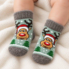 A close-up of a baby's feet wearing gray knit socks with a festive Christmas reindeer design, resting on a soft cream-colored blanket.