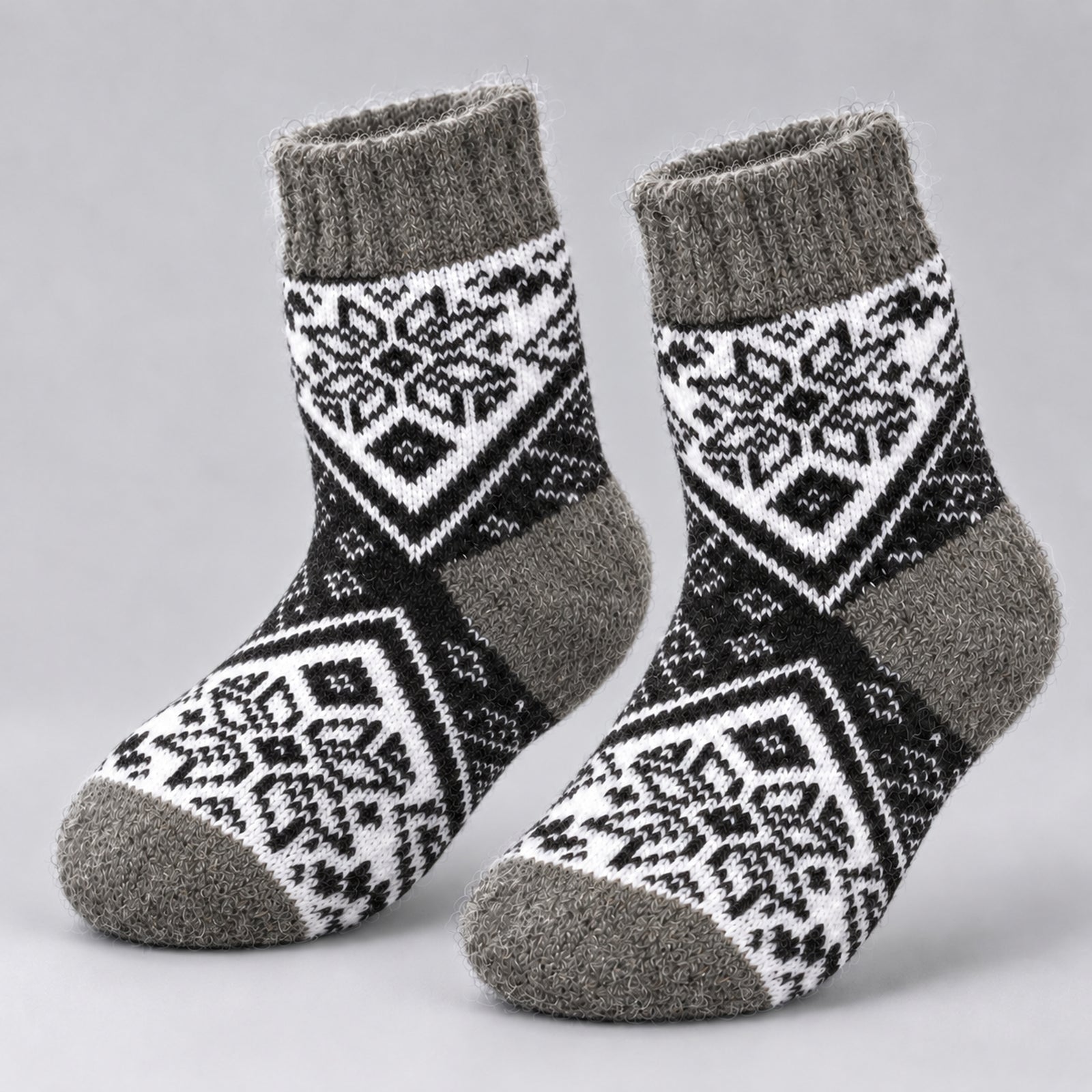 A pair of knit socks with a black and white geometric snowflake pattern and solid gray ribbed cuffs, heels, and toes, displayed on a light gray background.