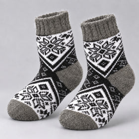 A pair of knit socks with a black and white geometric snowflake pattern and solid gray ribbed cuffs, heels, and toes, displayed on a light gray background.