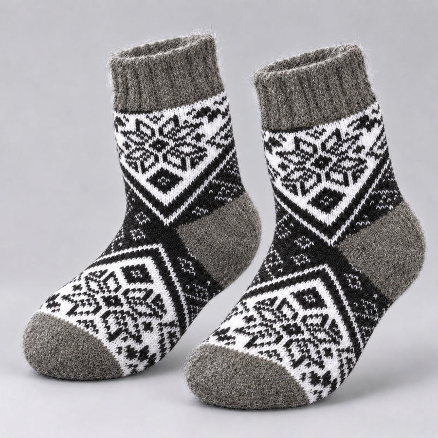 A pair of knit socks with a black and white geometric snowflake pattern and solid gray ribbed cuffs, heels, and toes, displayed on a light gray background.
