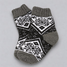A pair of knit ankle socks with a black and white geometric Fair Isle pattern and solid gray ribbed cuffs, heels, and toes, displayed on a neutral gray background.