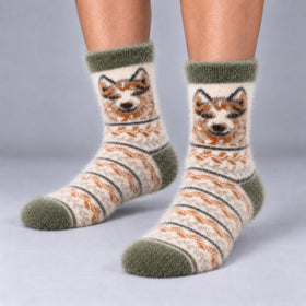 A pair of fuzzy knit socks worn on a person's feet, featuring a fair isle-style design with a dog face motif in brown and cream, olive green cuffs, heels, and toes, and thin dark gray stripes.