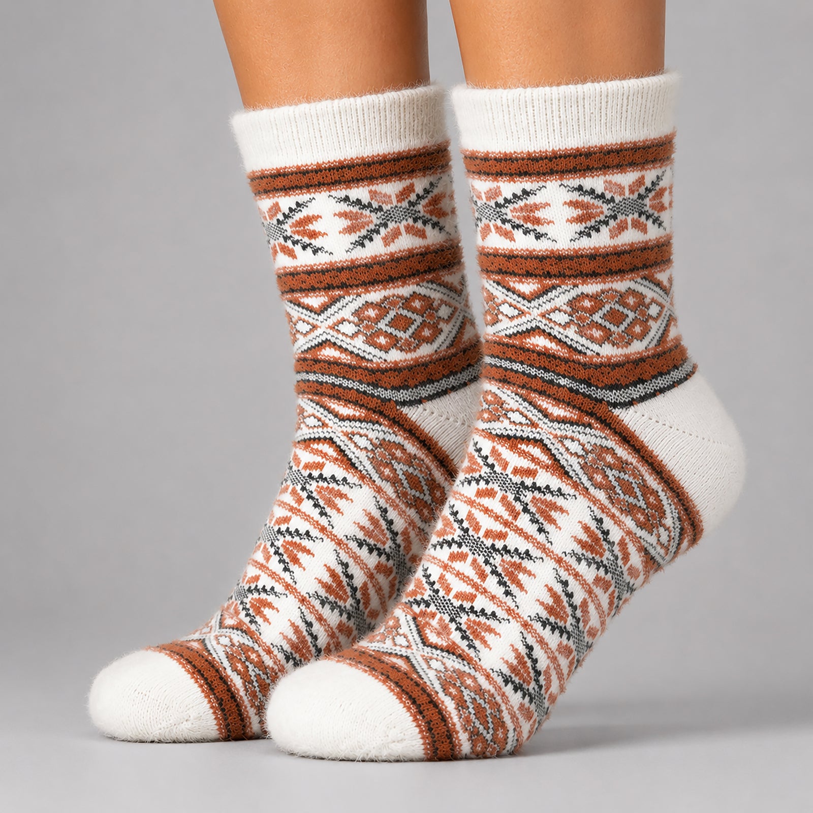 A pair of crew socks with a Southwestern geometric pattern in rust orange, gray, and white, shown on a person's feet against a solid gray studio background.