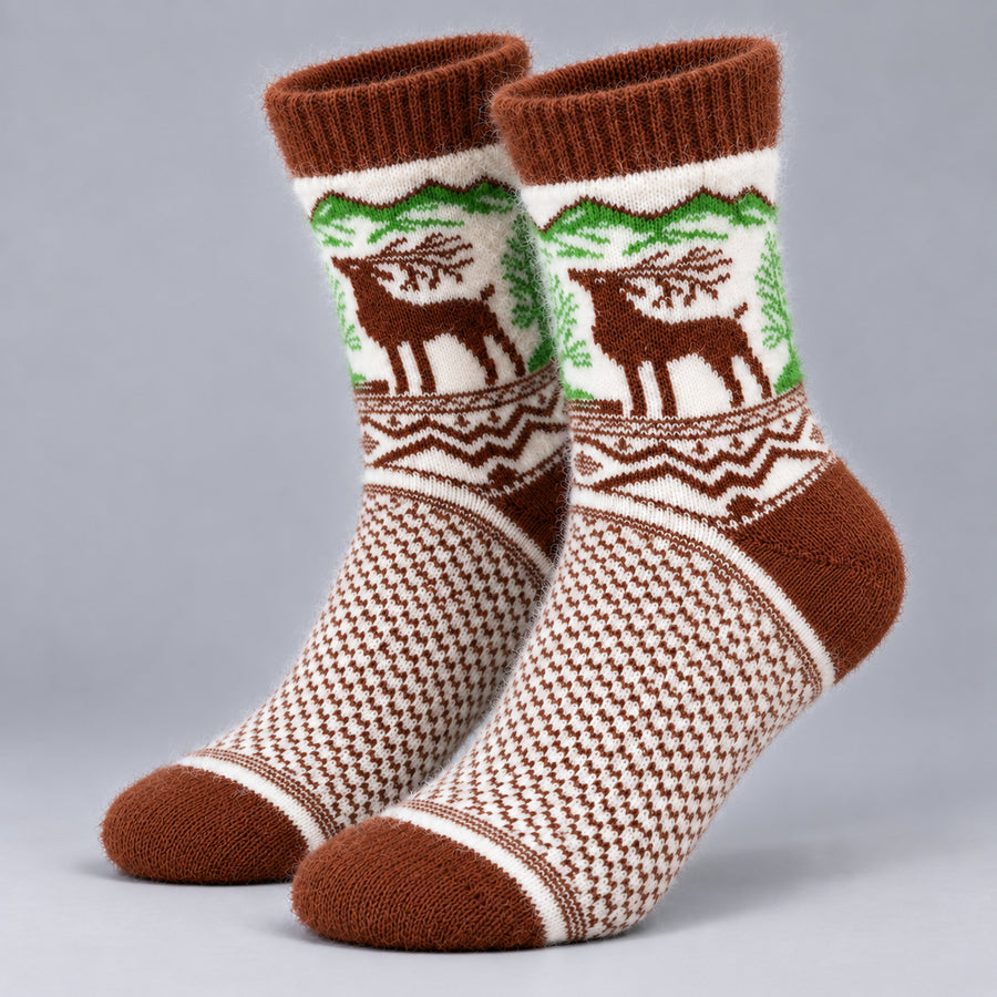 A pair of knit crew socks with a brown and cream geometric pattern, green pine tree motifs, and brown reindeer silhouettes, displayed against a neutral gray background.