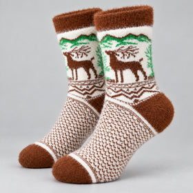 A pair of fuzzy knit socks with a brown and cream pattern, featuring a green forest and brown deer design on the upper leg, set against a plain light gray background.