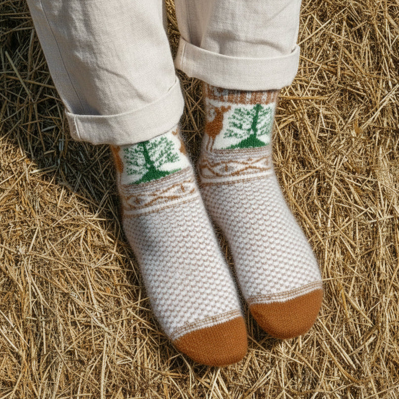 Knitted socks with a forest design on a person standing on hay.