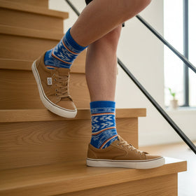 Person wearing brown shoes and blue patterned socks climbing wooden stairs.