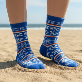 Blue patterned socks on feet standing on a sandy beach with ocean view