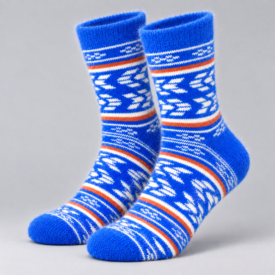 A pair of blue knit socks with white and orange Nordic-style geometric patterns, displayed against a neutral gray background.