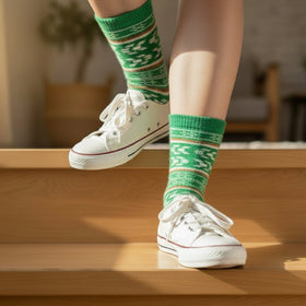 Person wearing green patterned socks and white sneakers on a wooden floor.