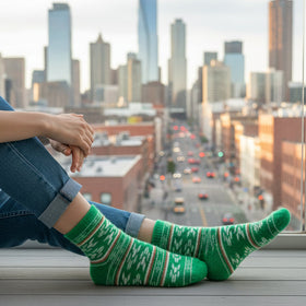 Person wearing green socks with a cityscape view from a high-rise window.