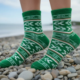 Green patterned socks on a person standing on a pebbly beach.