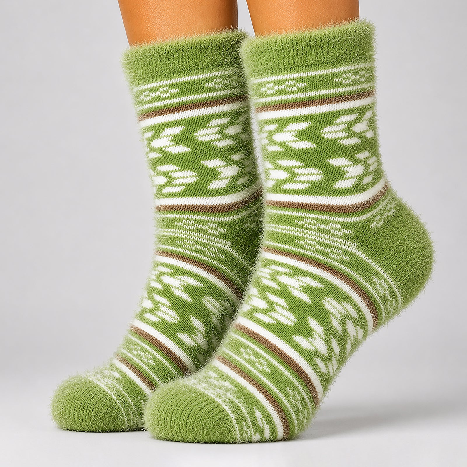 A pair of fuzzy knit socks in olive green with white and brown Fair Isle style patterns, shown on a person's feet against a light gray studio background.