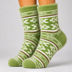 A pair of fuzzy knit socks in olive green with white and brown Fair Isle style patterns, shown on a person's feet against a light gray studio background.