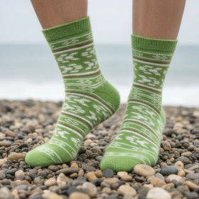 Green patterned socks on a person standing on a pebbly beach.