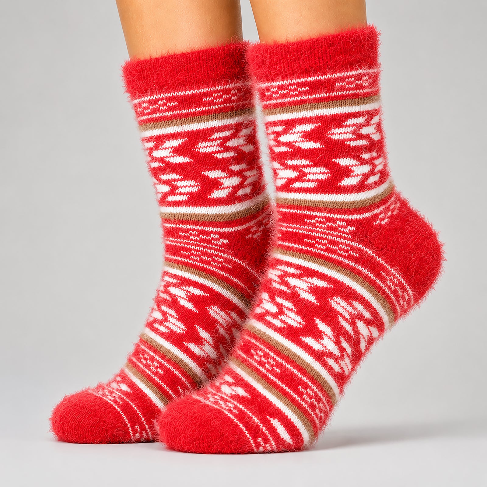 A pair of fuzzy red knit socks with white and tan geometric patterns, shown on a person's feet against a light gray studio background.