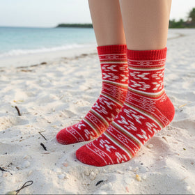 Red patterned socks on a person standing on a sandy beach.