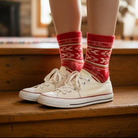 Person wearing red patterned socks and white sneakers on wooden steps.