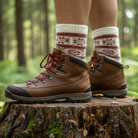 Person wearing brown hiking boots and patterned socks standing on a tree stump in a forest.