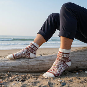 Person wearing patterned socks sitting on a log by the beach