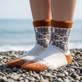 Person wearing patterned socks on a pebbly beach with ocean in the background